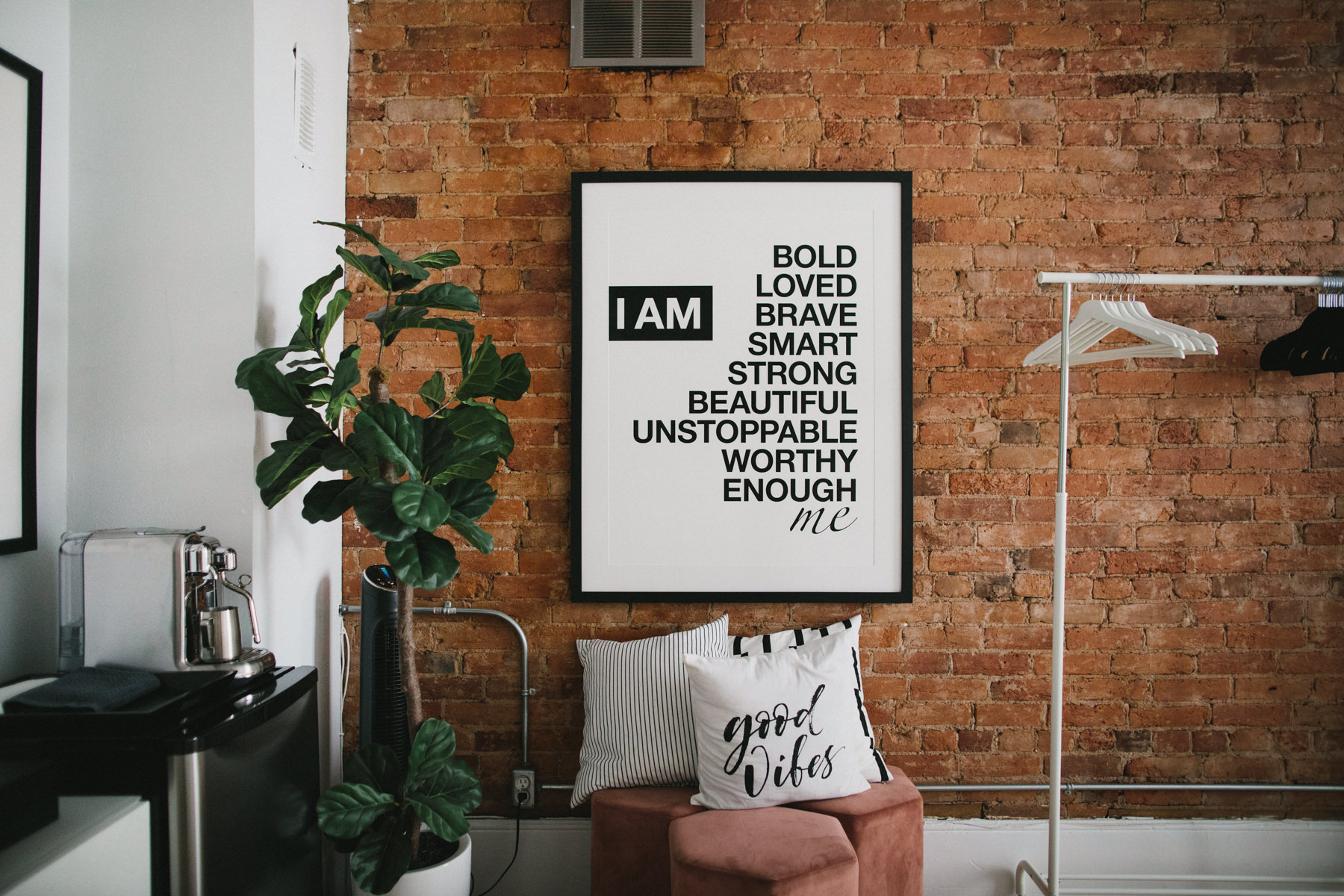 portrait studio hair and makeup room featuring a red brick wall and decorated with white furniture. Large wall art with a positive affirmation message is also featured.