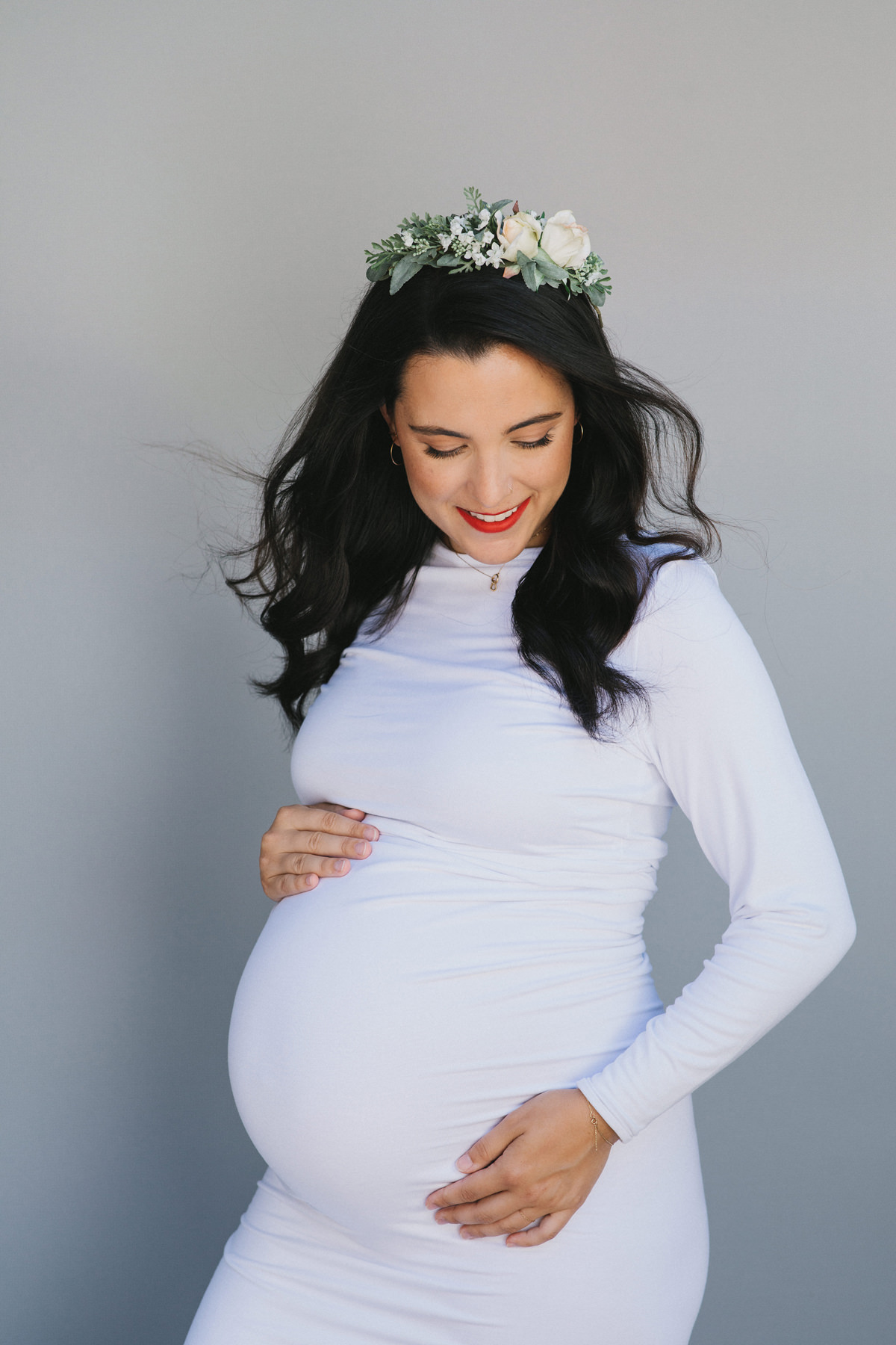 A boho style maternity portrait of a woman wearing a white body con dress.