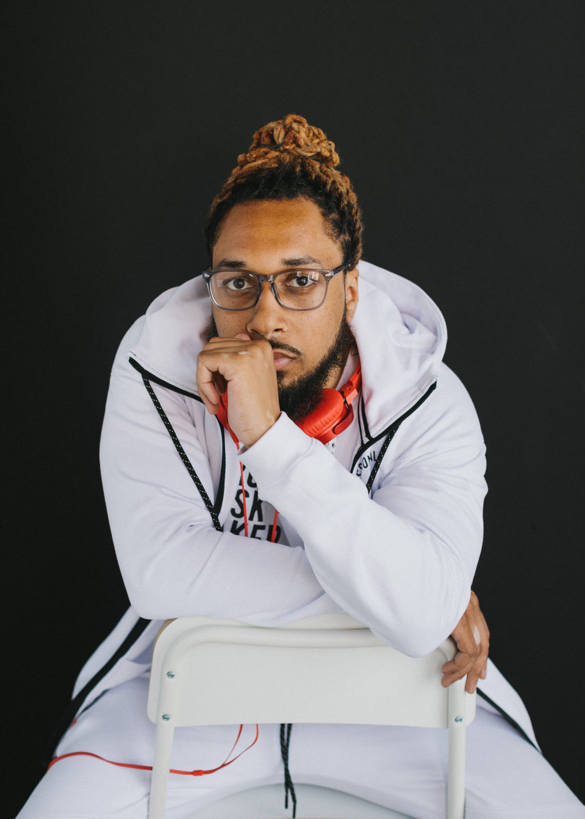 A branding portrait of a man in a white track suit seated in front of a black studio backdrop.
