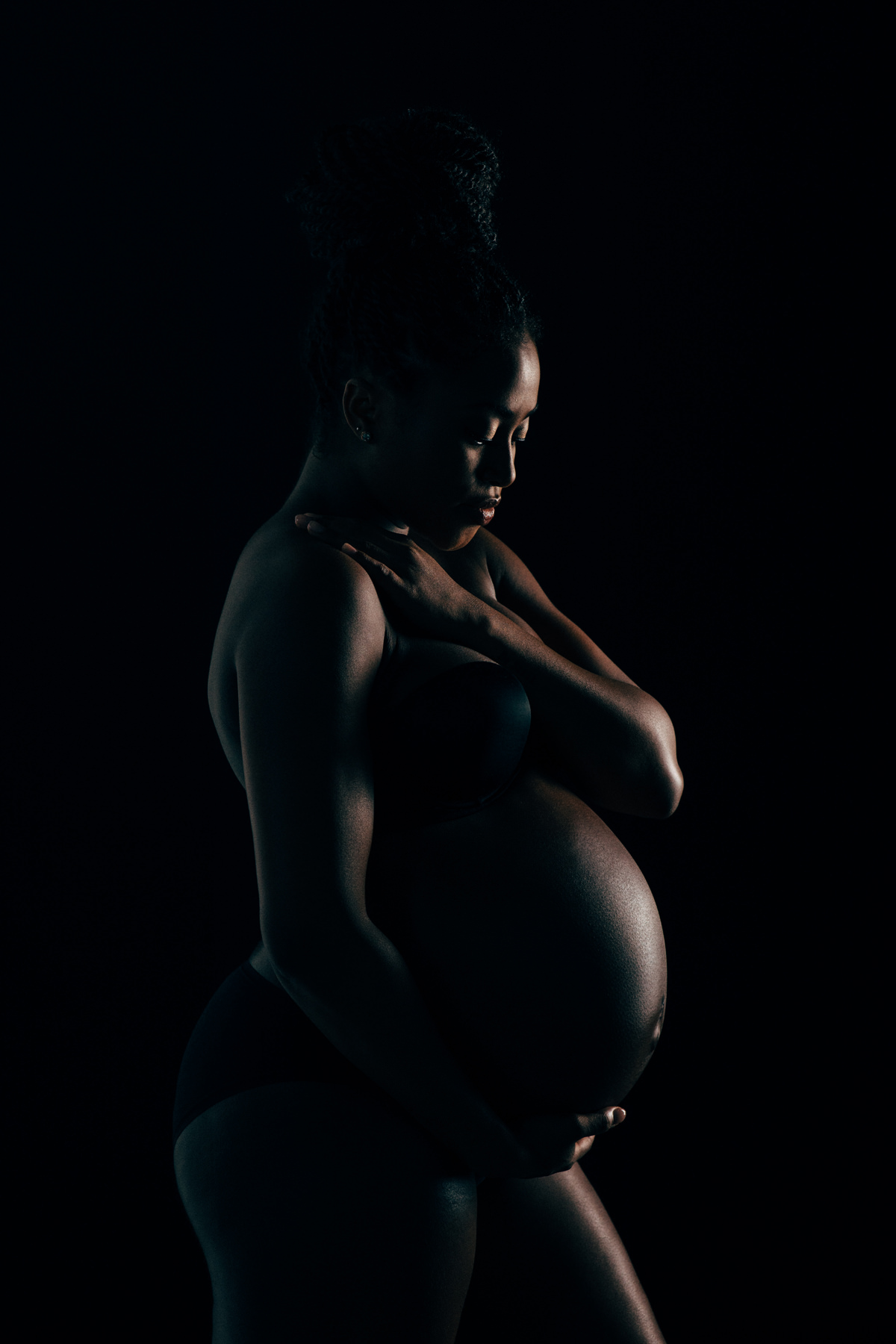 A creatively lit maternity portrait of a woman holding her pregnant tummy.