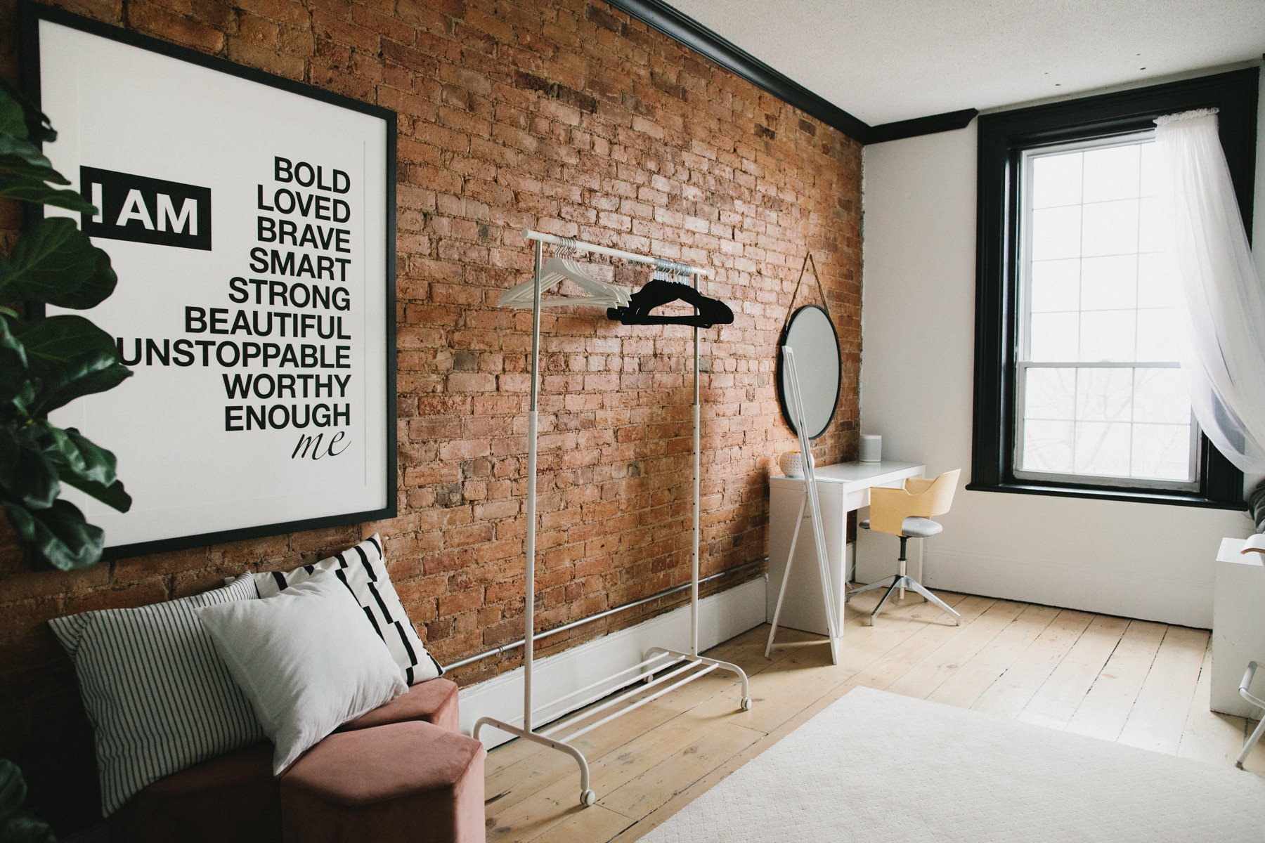 portrait studio hair and makeup room featuring a red brick wall and decorated with white furniture. Large wall art with a positive affirmation message is also featured.