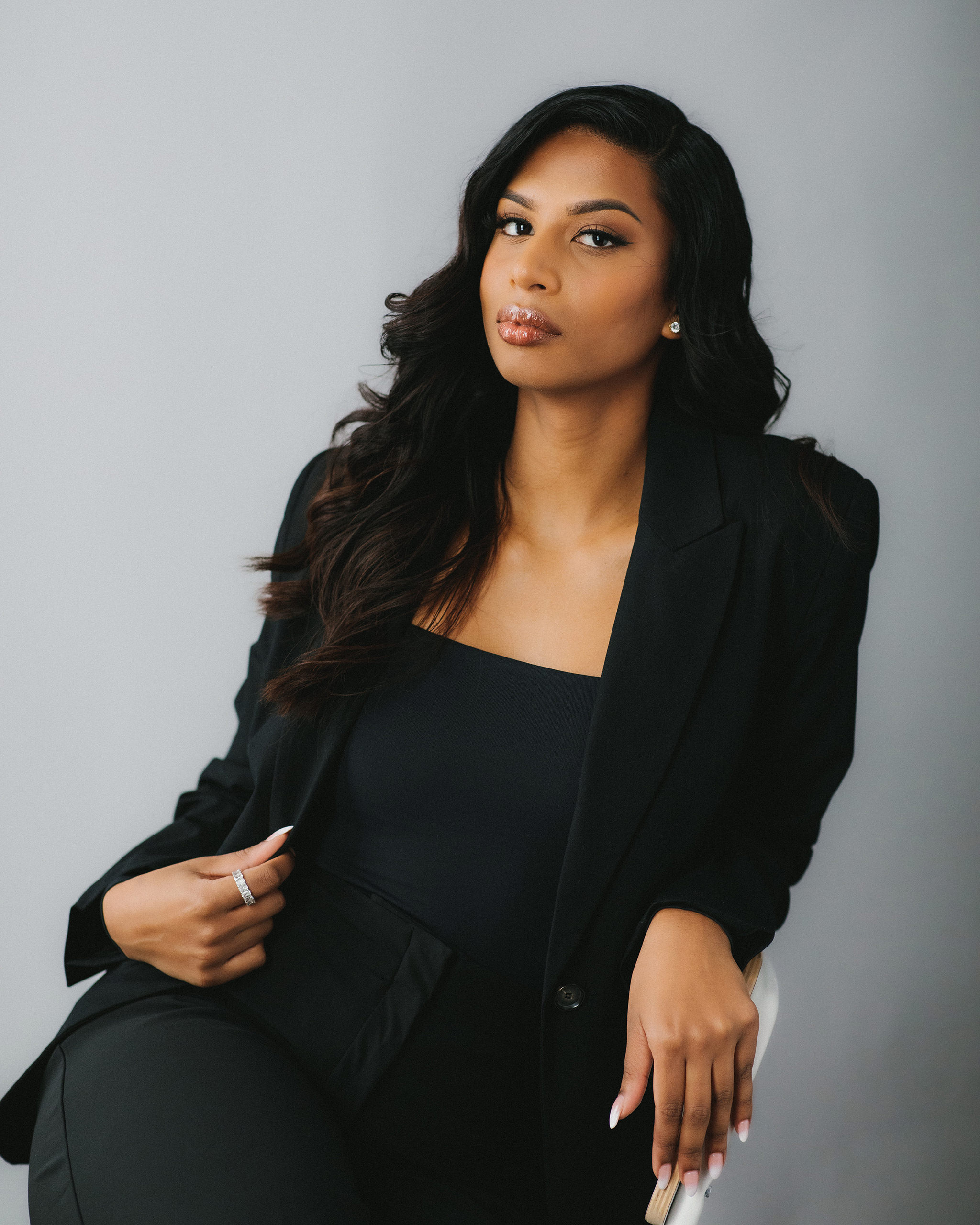 A portrait of a woman wearing a black suit and top, seated in a photography studio.