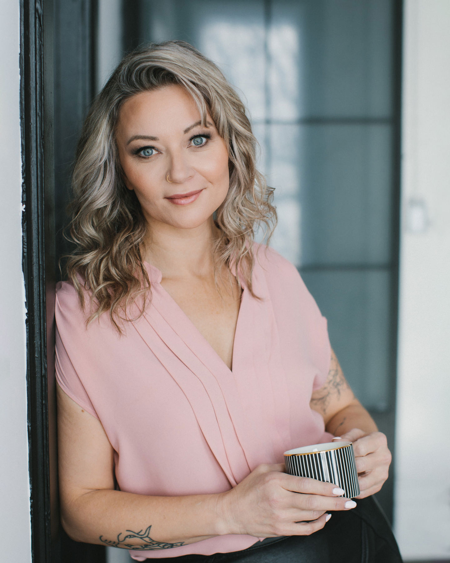 A casual branding portrait of a women in a pink sleeveless v neck top. She is holding a stripped mug.